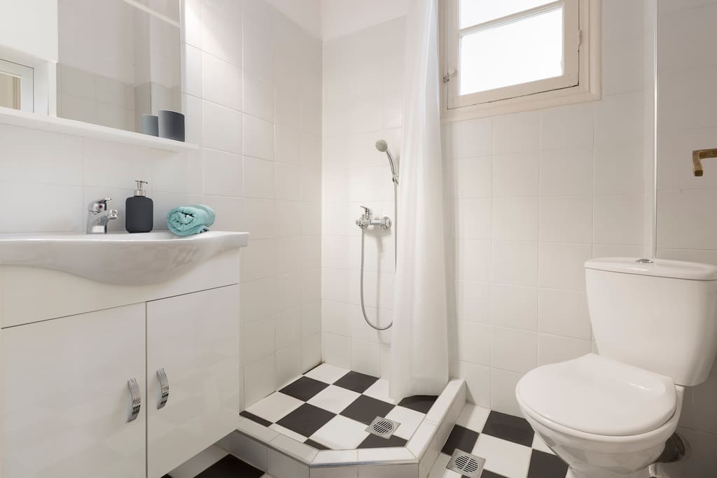 Comfortable toilet and shower with black and white floor tiles and big window to renew the air of the bathroom