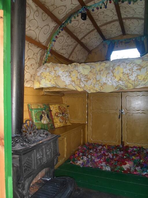 Inside the gypsy wagon, little log burner, large cupboard, one of the bench seats, and bed