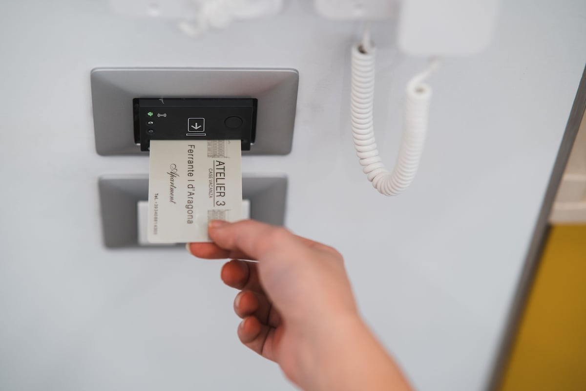 A hand is shown inserting a key card into a sleek electronic access panel. The panel features a minimalist design with a button and a small indicator light, contributing to a modern aesthetic in the entrance area.