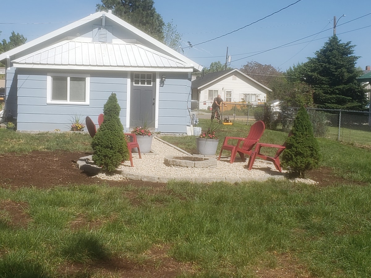 The exterior of the house features a well-manicured yard with a small gravel area surrounded by two red chairs and lush greenery. A fire pit is centrally located, offering an inviting outdoor space for relaxation.