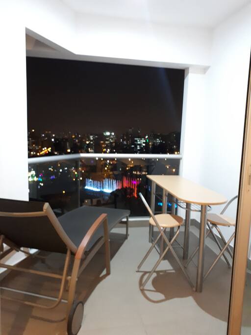 Balcón del dpto con silla chaise longue y mesita con 2 sillas para disfrutar la vista del Parque