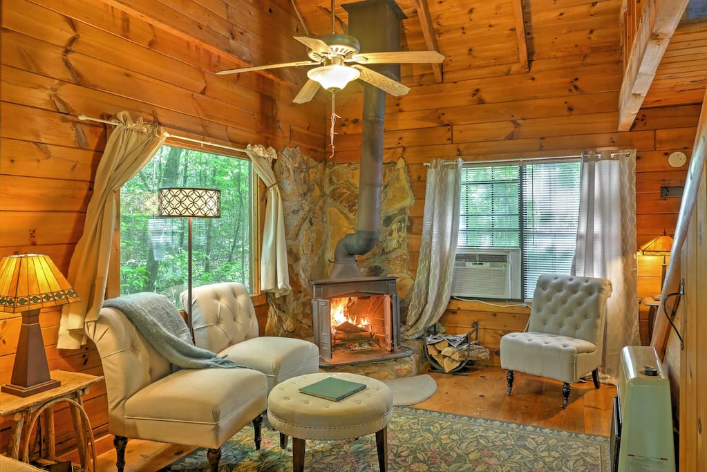 Rustic wood paneling throughout, a wood-burning fireplace, and cozy, plush furnishings create a warm environment.