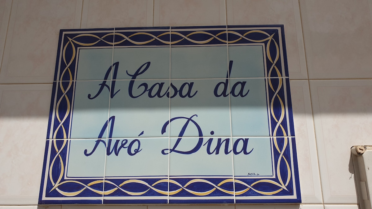 A decorative tile plaque displaying the words "A Casa da Avó Dina" is featured prominently on a light-colored wall. The plaque is framed with a blue and gold border, highlighting its significance as a welcoming marker for the property.