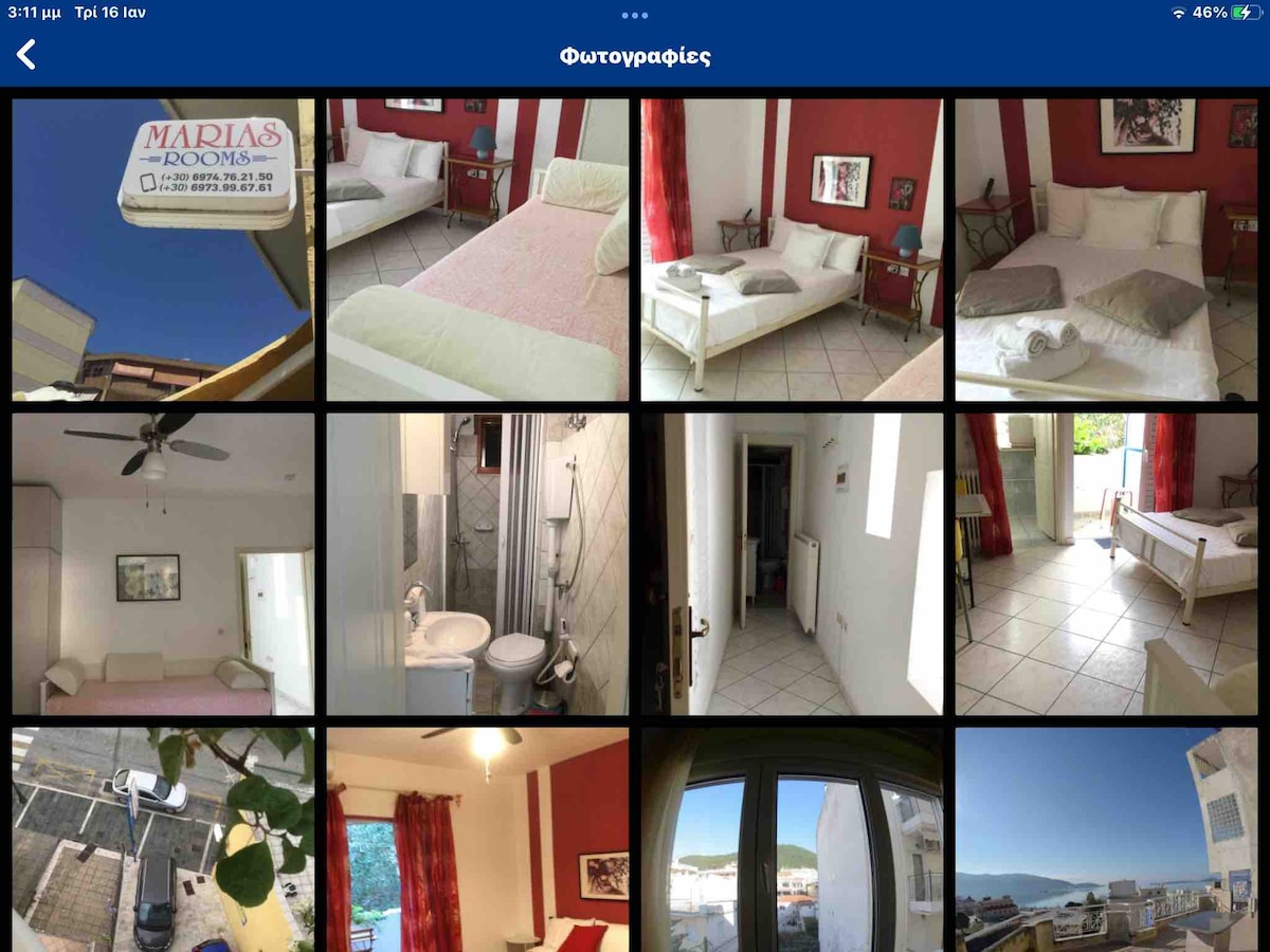 A welcoming studio room features a spacious bed and a balcony door that opens to enjoy fresh air. The bright red accents and neutral furnishings create a cozy environment. The bathroom area showcases a modern shower and tiled floors, designed for convenience.