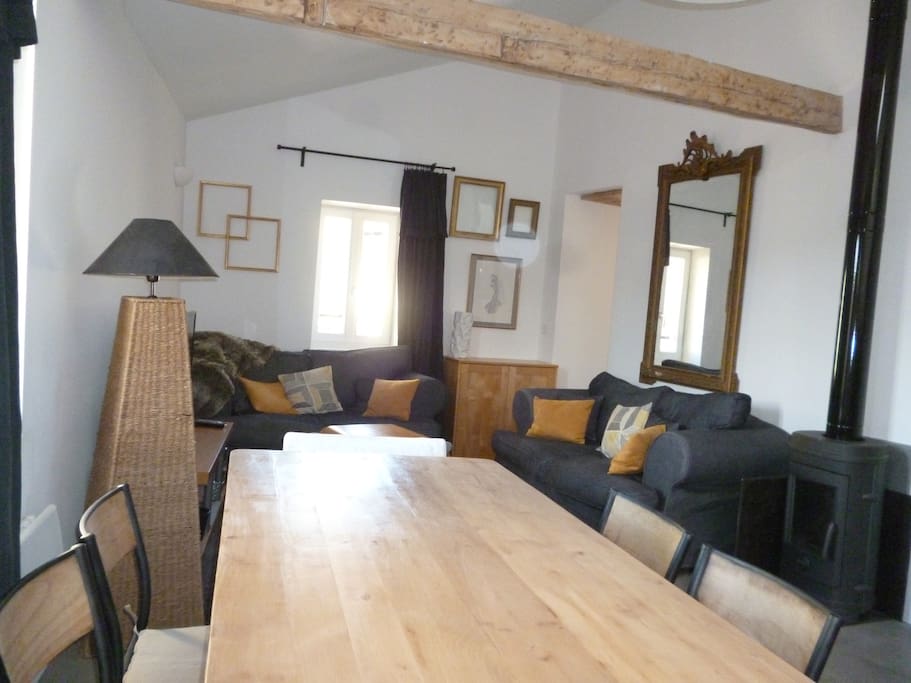 pièce principale vue sur salon avec table de ferme, poêle à bois, double canapé, TV