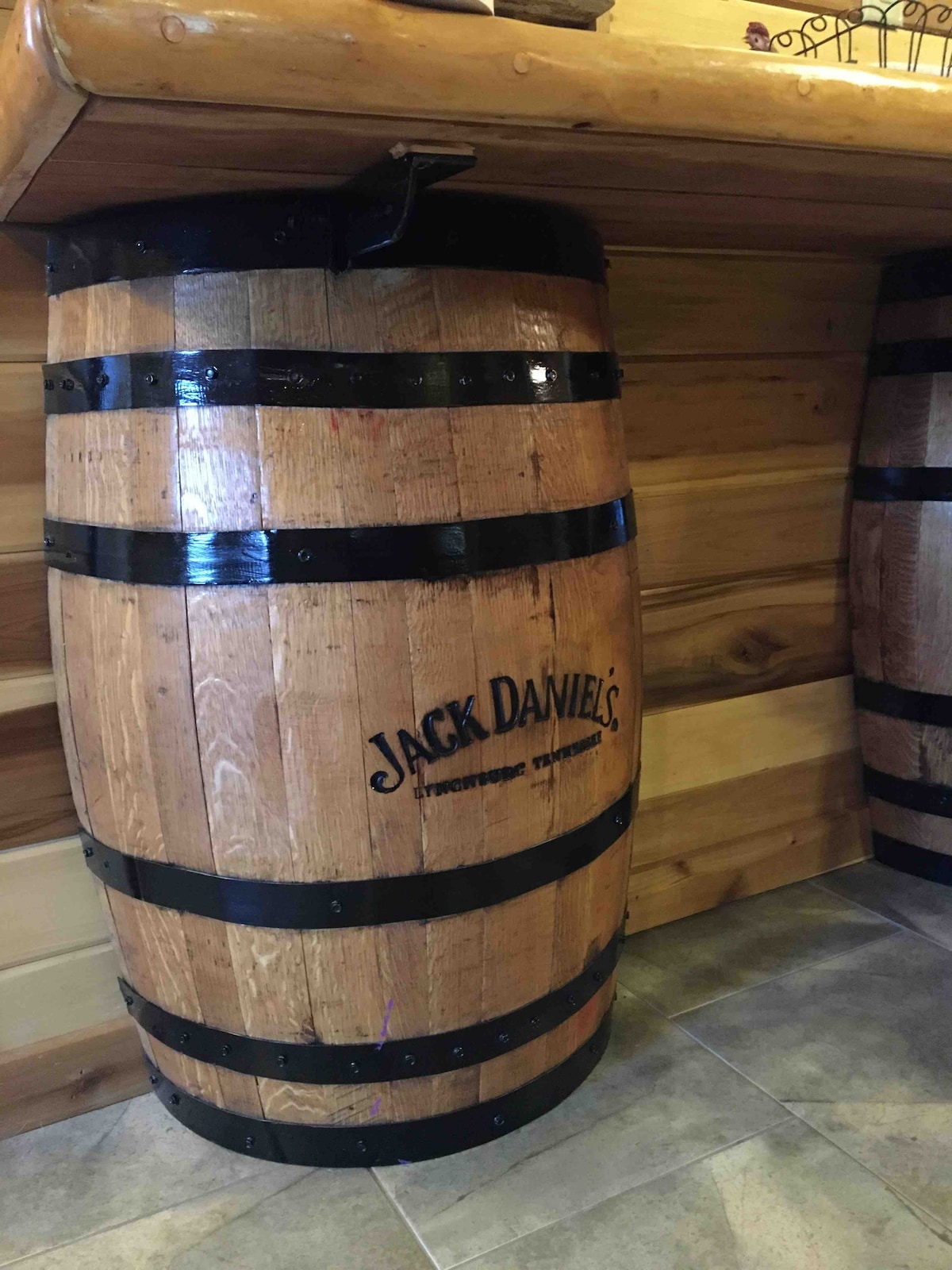A wooden barrel with dark metal bands displays the Jack Daniel's logo prominently. The barrel stands against a backdrop of wooden paneling, contributing to the rustic ambiance of the space.