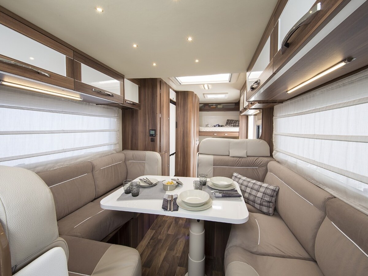 An inviting dining area is featured, showcasing a light-colored table surrounded by plush, beige seating. Natural light filters through layered window coverings, creating a cozy setting. Dinnerware is neatly arranged on the table, complemented by decorative accents in subtle tones.