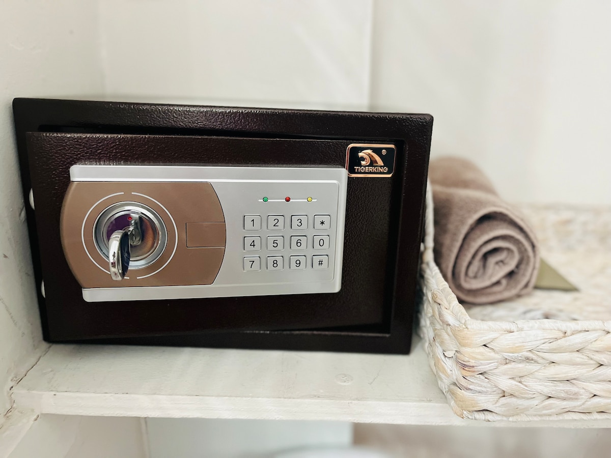 A hotel-grade safe is positioned on a shelf, featuring a keypad for secure access. A folded towel rests beside it, and a woven basket holds additional items, enhancing the organized ambiance of the space.