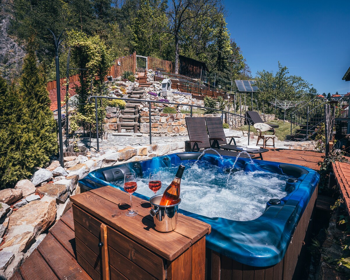 A hot tub is positioned on a wooden deck, surrounded by a well-maintained garden with lounge chairs. Stone pathways lead to terraced areas filled with greenery, enhancing the outdoor space for relaxation.