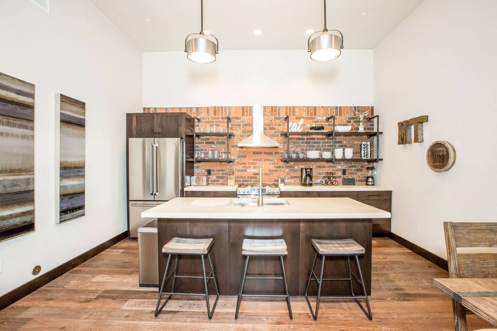 Open kitchen has stunning concrete countertops, brick backsplash & 3 barstools.