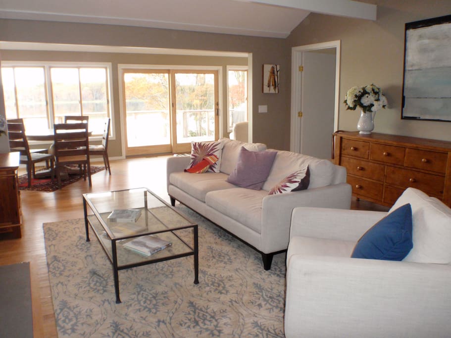 Sunny bright living room with fireplace, wall of windows overlooks water