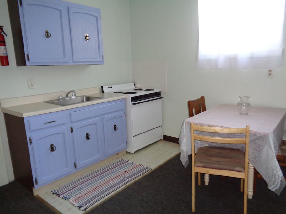 separate kitchen with dishes and pots in cabinets, sink, stove, oven, kitchen table and chairs