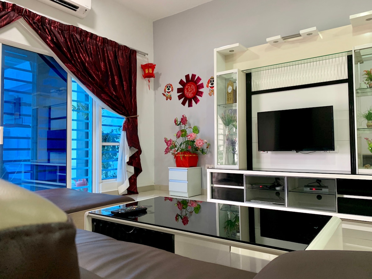 A modern living area is highlighted by a sleek black coffee table and an elegant white entertainment unit with a flat-screen TV. Colorful wall decor and a potted plant add a touch of vibrancy, while large windows allow natural light to fill the space.