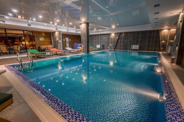 An indoor pool is surrounded by a tiled deck with several lounge chairs resting at the edges. Soft lighting reflects off the water's surface, creating a calming ambiance. Large windows provide visibility to adjacent areas, enhancing the overall openness of the space.