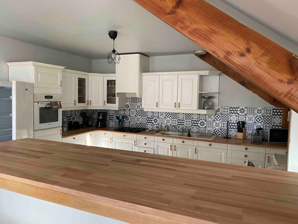 The kitchen features modern cabinetry and a tile backsplash with a geometric pattern. Equipped with essential appliances, including an oven, stove, and coffee maker, the space is designed for functionality. A wooden countertop provides a large surface for meal preparation.
