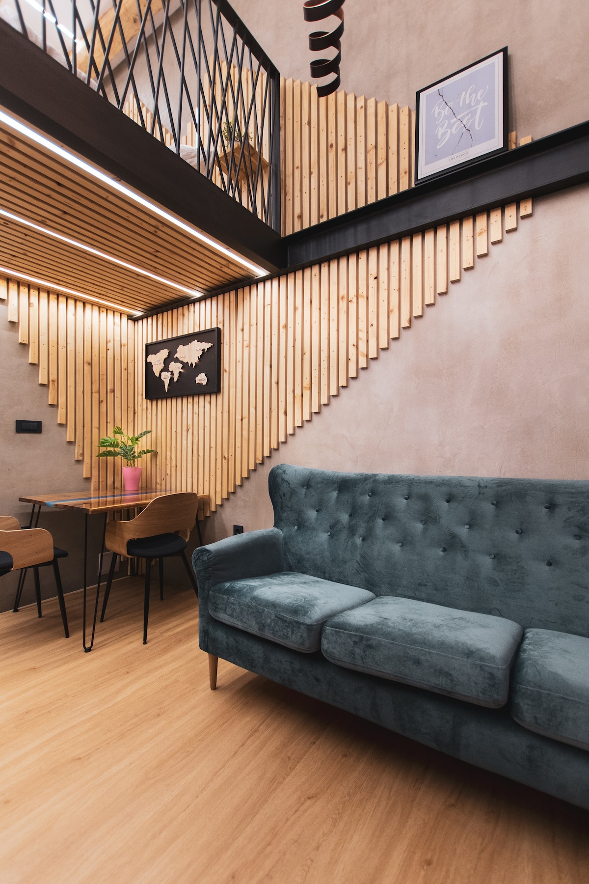 A cozy living space features a plush blue-green couch and a wooden dining table surrounded by four chairs. Natural wood paneling decorates the walls, creating a warm ambiance. An attractive wall art piece adds a touch of character. Soft lighting enhances the inviting atmosphere.