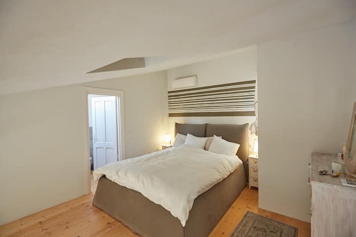 La chambre dispose d'un lit confortable (160x200) avec un ensemble de deux couettes et quatre oreillers. À gauche, vous voyez la porte de la salle de bain supérieure. La climatisation est disponible dans les deux chambres à l'étage.