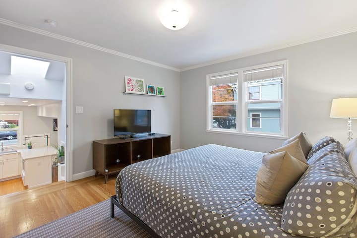 غرفة نوم رئيسية مع تلفزيون بشاشة مسطحة ونوافذ.