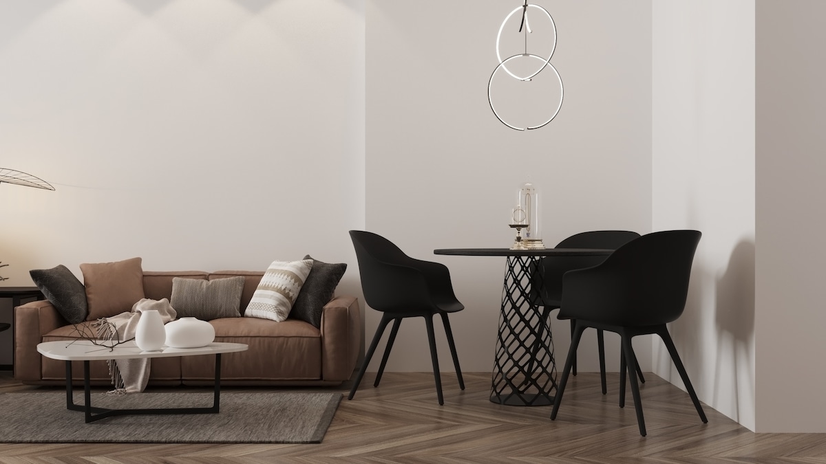 A modern living space features a cozy brown sofa adorned with decorative pillows. A round dining table with black chairs is positioned nearby. Soft lighting creates a calming ambiance, highlighting the minimalist design and wood flooring.
