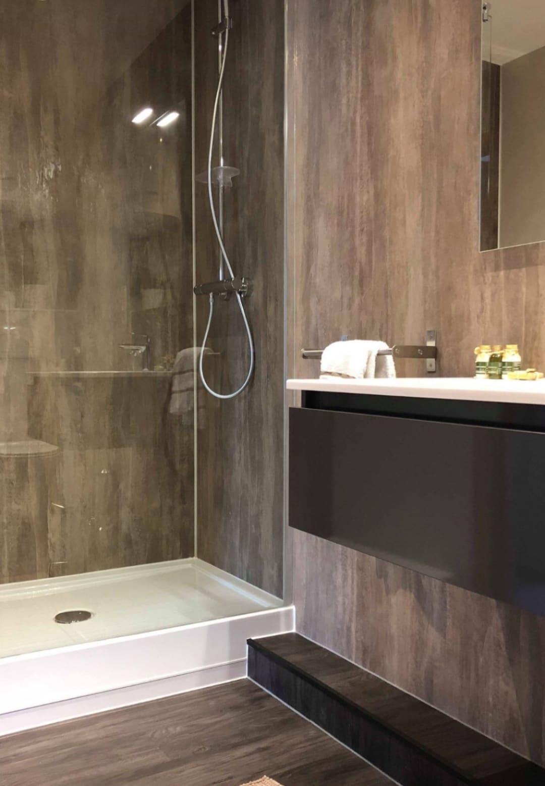 A modern bathroom features a walk-in shower with a clear glass enclosure, showcasing a sleek design. A black vanity with a minimalist sink is positioned beside it. Towels and complimentary toiletries are neatly arranged on the counter, adding functionality to the space.
