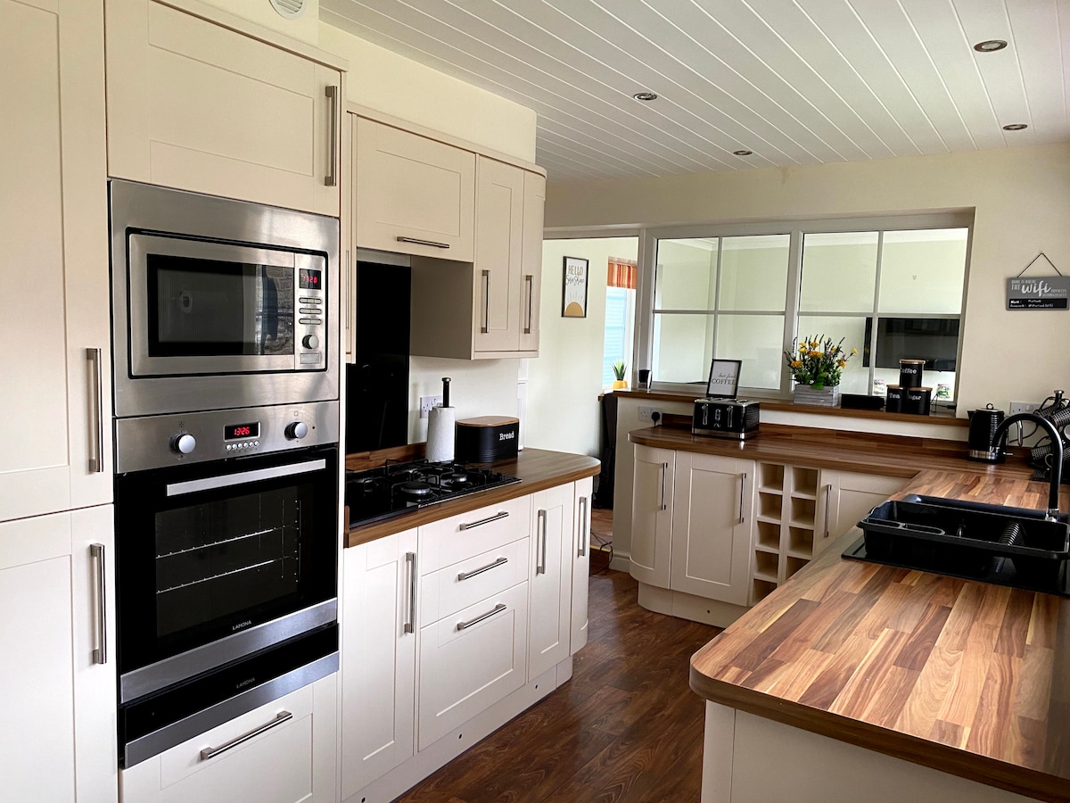 A modern kitchen is equipped with a stainless steel oven, built-in microwave, and a gas cooktop. Light-colored cabinetry complements the wood countertops. Abundant natural light enters through nearby windows, illuminating the space, while convenient appliances and a spacious layout promote a welcoming cooking environment.