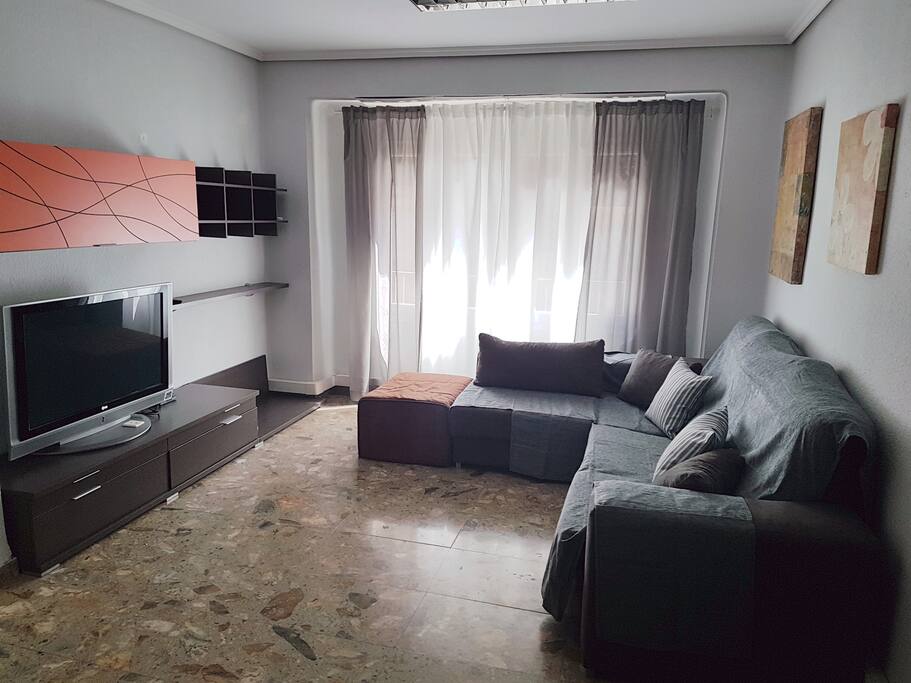 Salón- comedor. Sofá chaise lounge, televisión de plasma, espacio de alamacenaje y aire acondicionado.