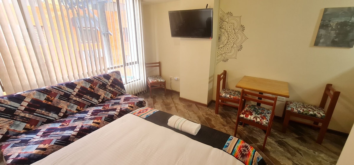 A comfortable sleeping area is organized with a spacious bed, complemented by colorful patterned bedding. A small wooden table is set near the couch, which features a vibrant fabric covering. A flat-screen TV is mounted on the wall, enhancing the room's functionality.