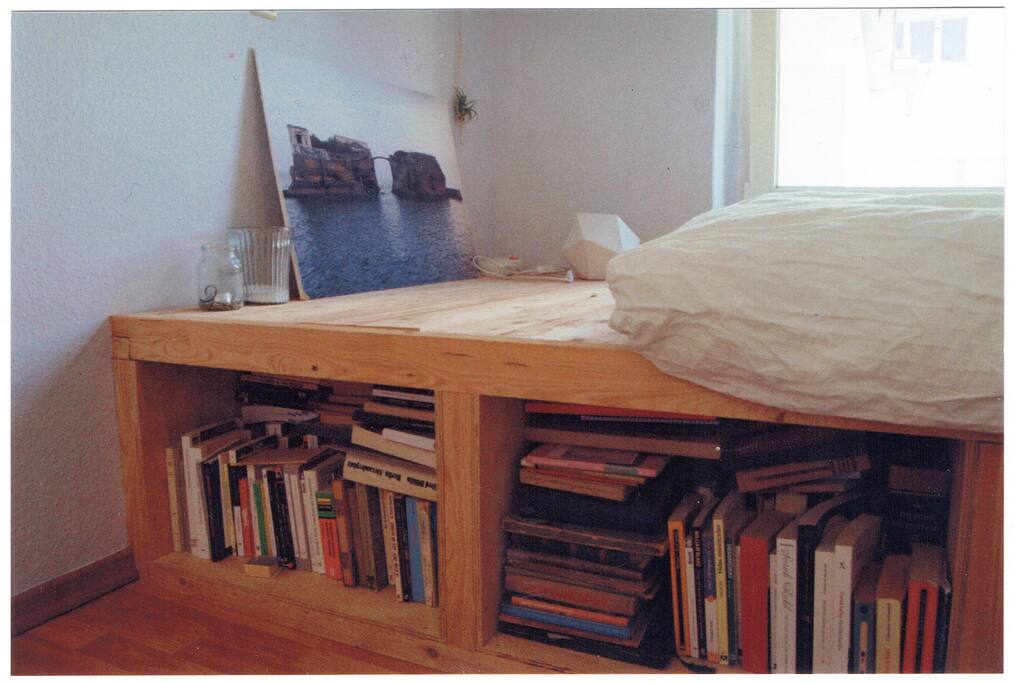 Cosy double bed on a wooden structure next to the window