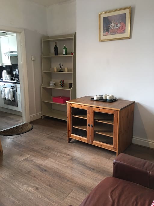 Livening room has dinning table, chairs, fridge, freezer, leather armchair, tea set and tea bags.