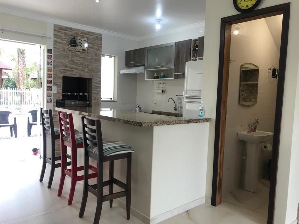 A modern kitchen space is presented with a granite breakfast bar featuring three high-backed stools. Sleek cabinetry and appliances are visible, accompanied by a stone accent wall. An open doorway leads to a small outdoor area, enhancing the natural light in the kitchen.