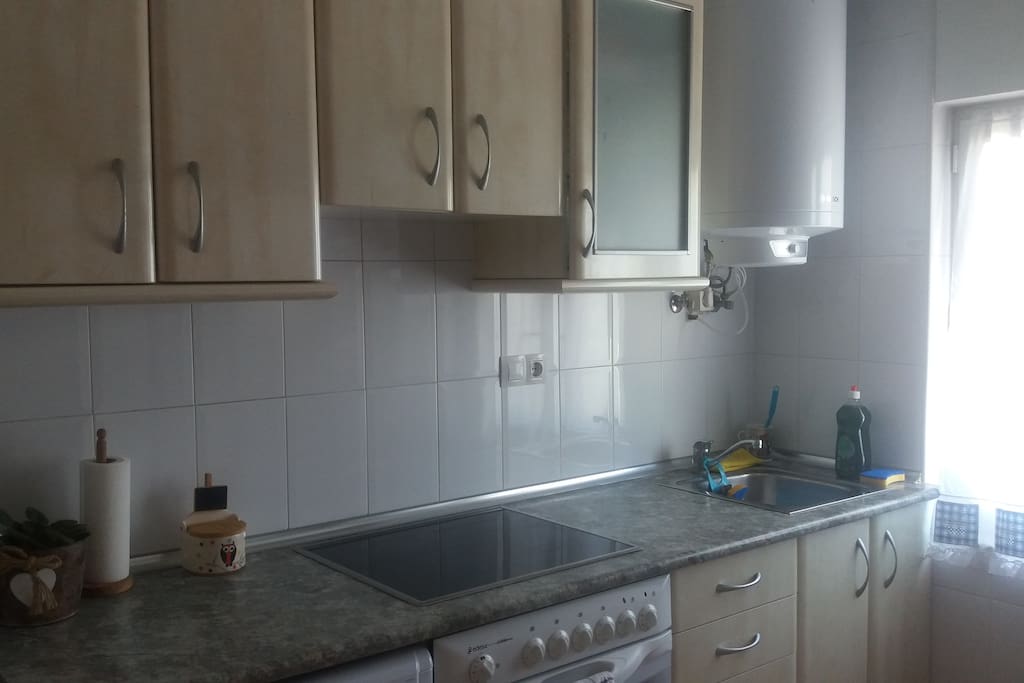 Cocina con lavadora, frigorífico, vitrocerámica y termo de agua.