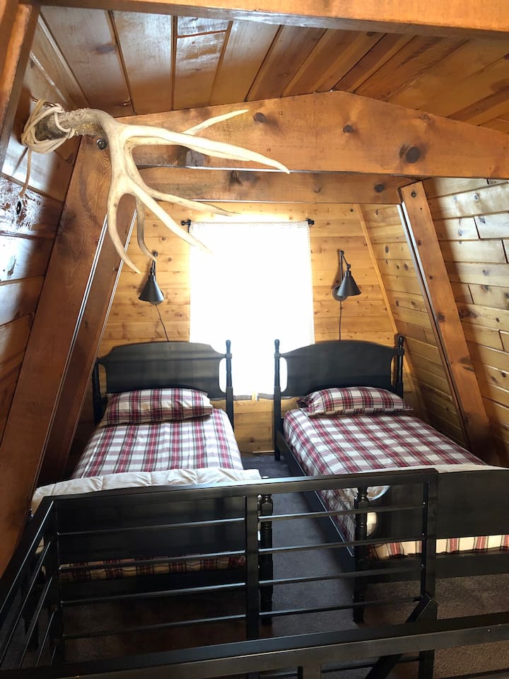 Два двокреветни кревета скриени во мало катче што создава чувство на спиење во куќа на дрво.