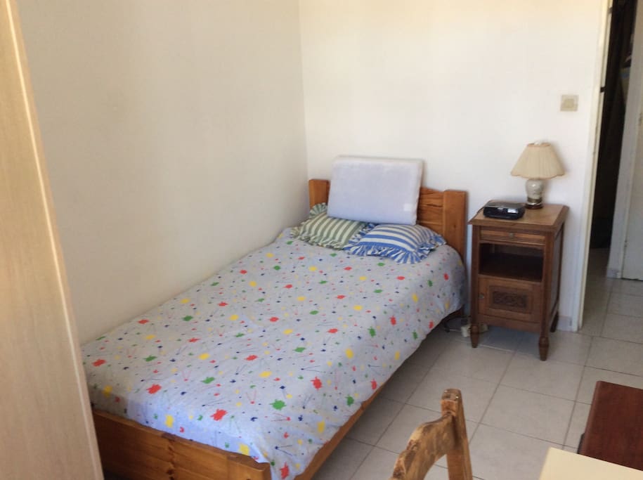 Chambre avec un lit à une place , table de nuit, armoire, bureau,une fenêtre rendant la chambre lumineuse
