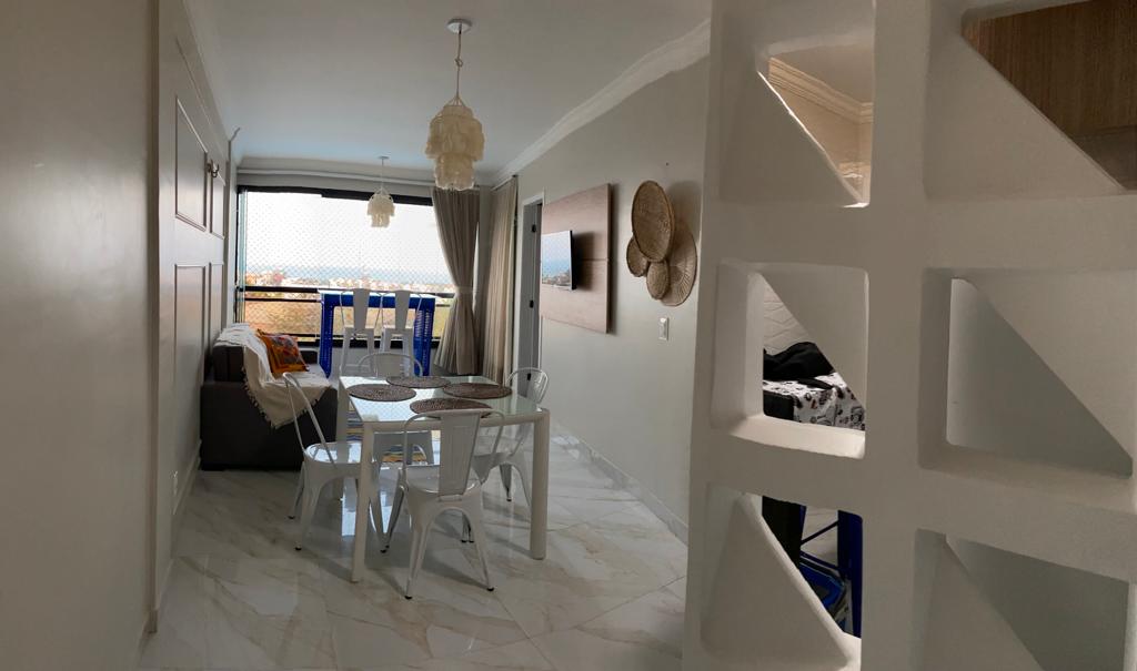 A modern indoor space is showcased, with a cozy seating area featuring a gray sofa and white dining table surrounded by four chairs. Large windows allow natural light to fill the room, and a balcony is visible in the background, offering views of the outside.