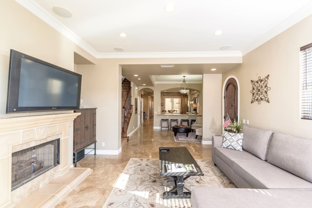 1st floor great room; front living/entertainment space off front patio; sitting area, kitchen, stairway to upper floors, middle patio; big screen TV and gas fireplace; stone floors; granite counters; half-bath
