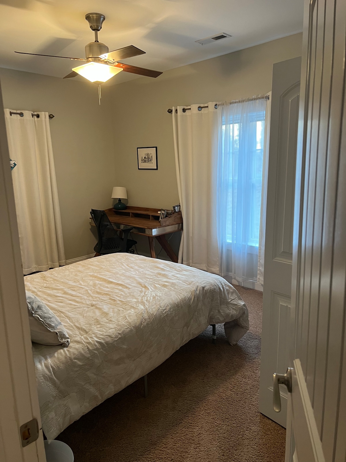 Front bedroom with queen size bed, desk workspace, closet, blackout curtains on both windows, ceiling fan. 