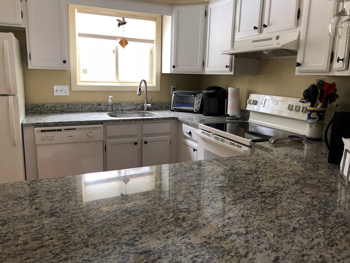 A well-equipped kitchen showcases granite countertops, white cabinetry, and modern appliances. Natural light enters through a window, illuminating the sink area and providing a functional space for meal preparation.