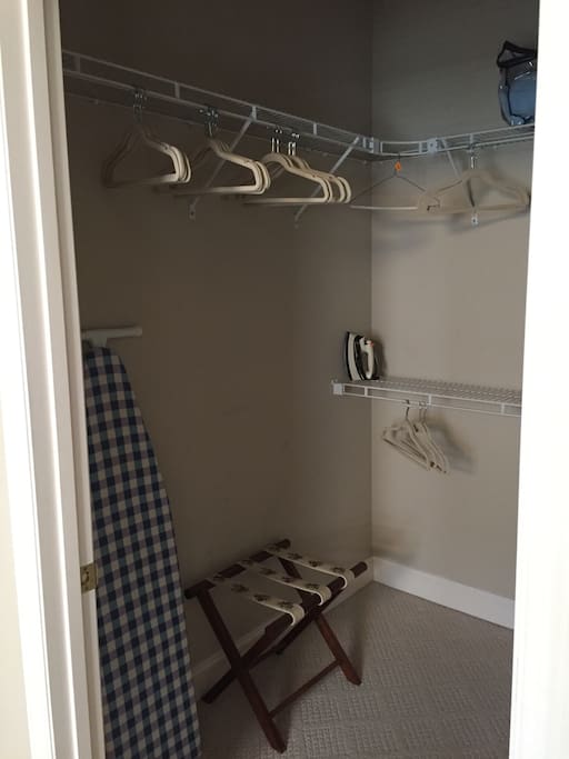 Large walk-in closet with suitcase rack, hangers, iron, ironing board and spray starch.