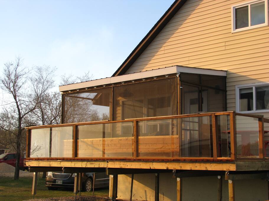 The lakeside deck has the screened room that leads out to open deck space with glass railings and a round table and benches perfect for relaxing while watching the sunset over the water.