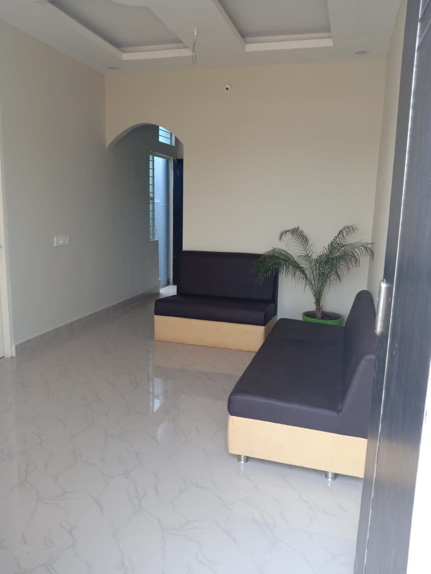 A bright and airy entryway features two modern seating areas with dark upholstery set against light-colored walls. The polished floor reflects the natural light coming from a nearby window, while a small potted plant adds a touch of greenery to the space.