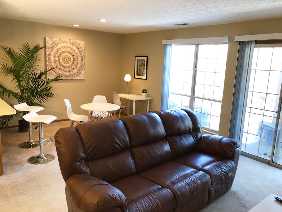Open concept living room with light-filled windows overlooking private patio, comfy leather couch, dining area, and a desk with super fast WiFi internet.