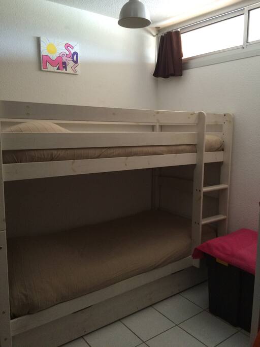 Chambre avec lits superposés, équipée d'un grand placard, d'une fenêtre.