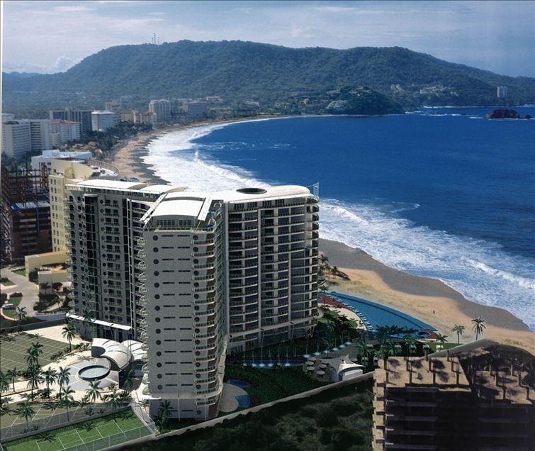 An aerial view of a modern beachfront condo complex is showcased, with several floors and circular architectural features. The surrounding landscape includes sandy beaches and vibrant blue ocean waters. Lush palm trees line the property, enhancing the coastal setting against rolling hills in the background.