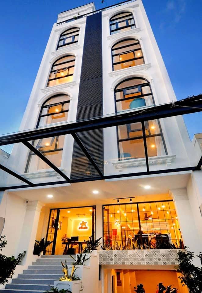 A modern building featuring an elegant facade with large arched windows is highlighted. The entrance showcases a stairway leading to an inviting lobby, illuminated by warm lighting. Lush greenery lines the pathway, enhancing the welcoming atmosphere of the space.