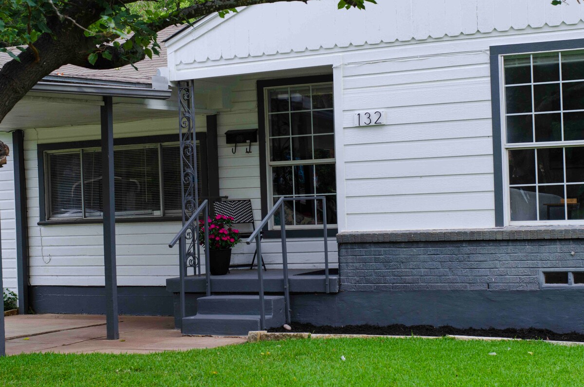 A charming house exterior is seen, featuring a welcoming porch with steps leading to the front door. A planter with flowers adds a touch of color, while large windows allow natural light to brighten the entryway. Well-maintained grass surrounds the area.