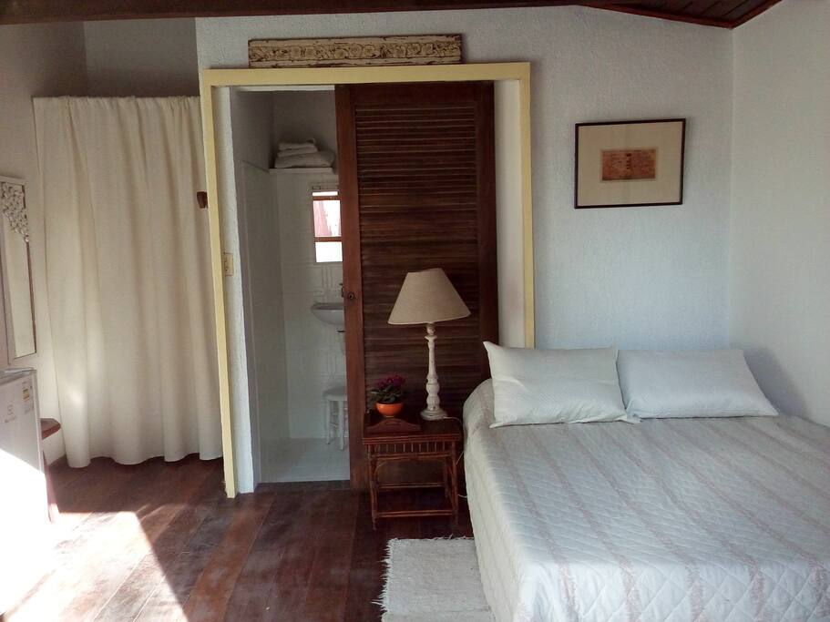 Vista principal da suite, com cama de casal, banheiro insuite, armário e frigobar.
