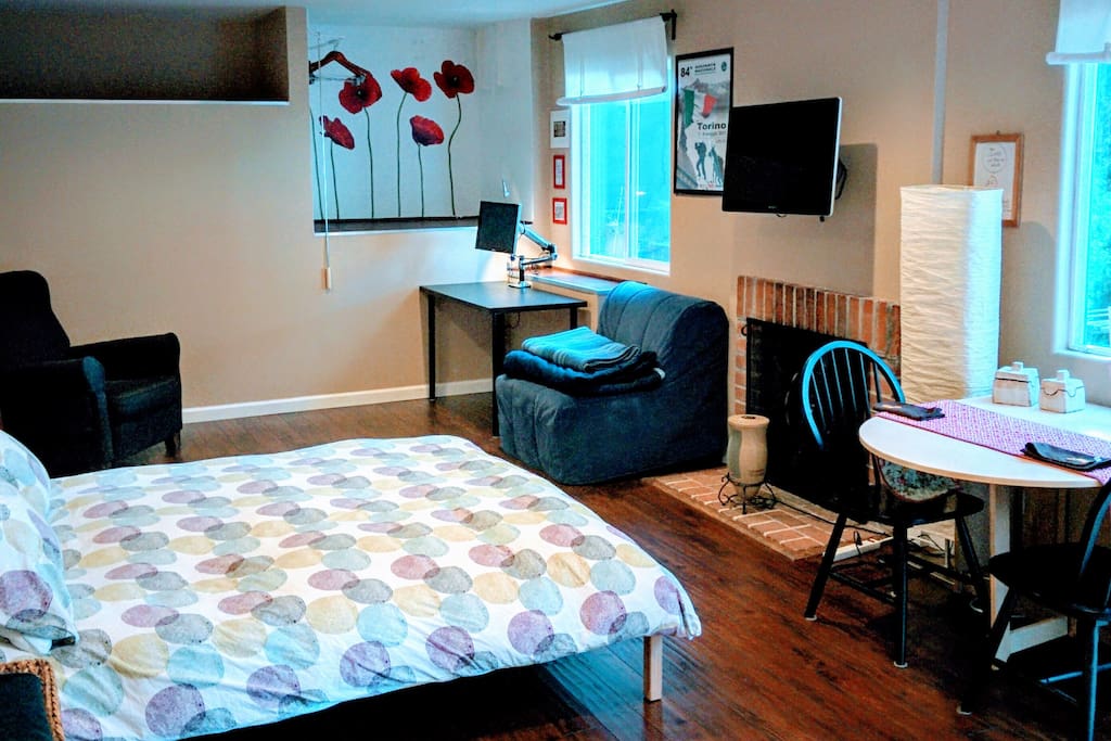 Main room. 300sft. Queen bed and blue armchair bed. Main room. View of the windows, desk, dining table and the fireplace
