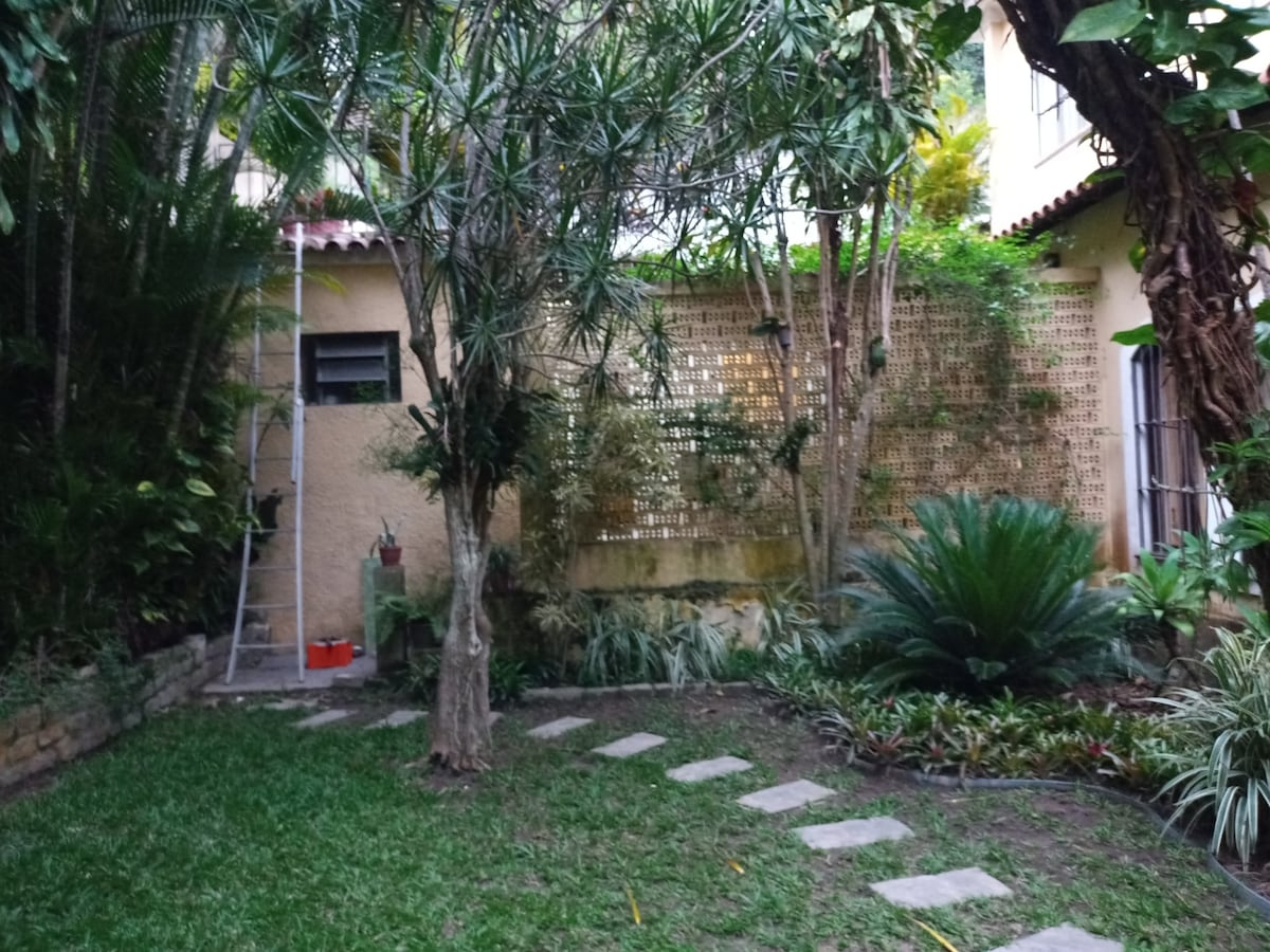 A serene garden setting is featured, with lush greenery surrounding a well-maintained lawn. Pathways of stepping stones lead through the garden, while a variety of plants contribute to a natural ambiance. A wall of vines adds texture and privacy to the space.