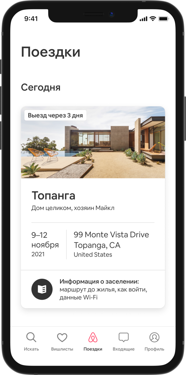 На экране мобильного телефона открыта вкладка «Поездки», в которой отображается предстоящая поездка. Под заголовком «Сегодня» видно изображение дома-шалаша, а под ним — детали бронирования: название объявления, имена хозяев, адрес и даты поездки. Внизу страницы есть кнопка: «Детали прибытия‎. Как добраться, как заселиться, данные Wi-Fi».