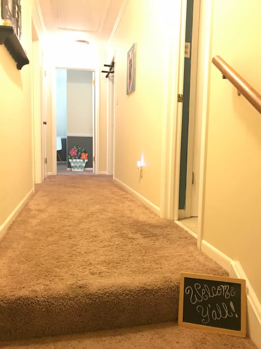 Bedroom is at end of first hall with a warm, flower basket welcome sign designator. The shared bathroom is the first door on the right (seen here to the right of the welcome y'all sign).